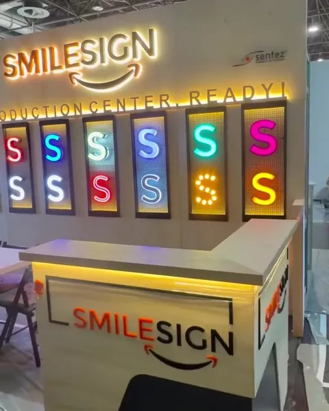 SmileSign stand at EuroShop 2026 in Düsseldorf: illuminated SmileSign logo, a wall of lit channel letter samples and the reception counter
