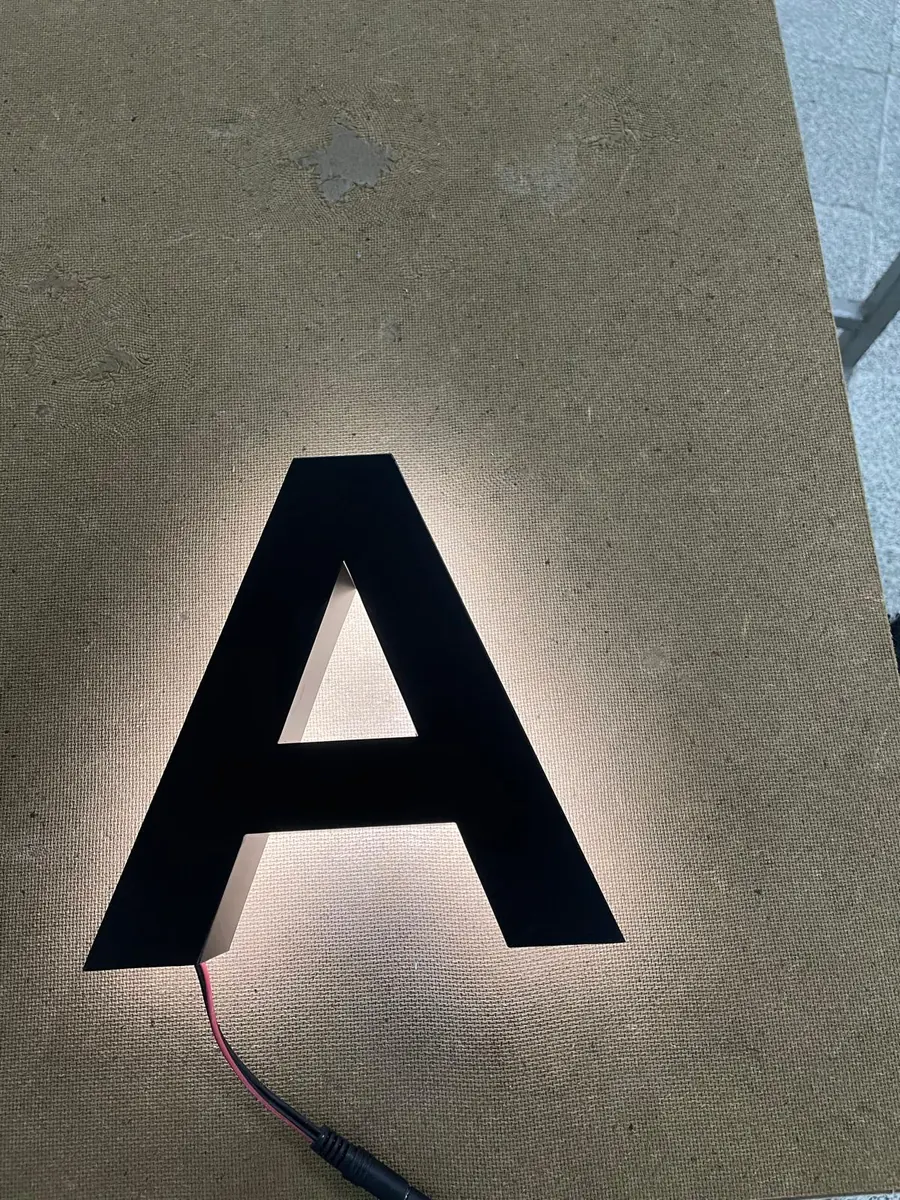 Indirect verlichte letter op een donkere wand, met licht dat gelijkmatig rond de randen uitstraalt
